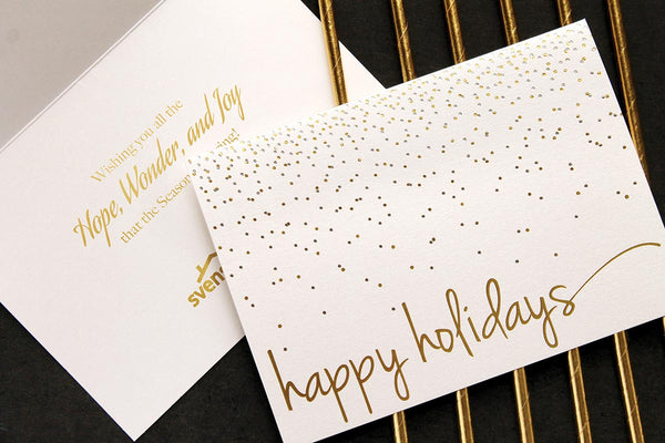 White pearlescent card on a black background highlighted with gold stripes has a gold and silver foil confetti design. Sentiment and company logo is gold foil stamped inside the card.