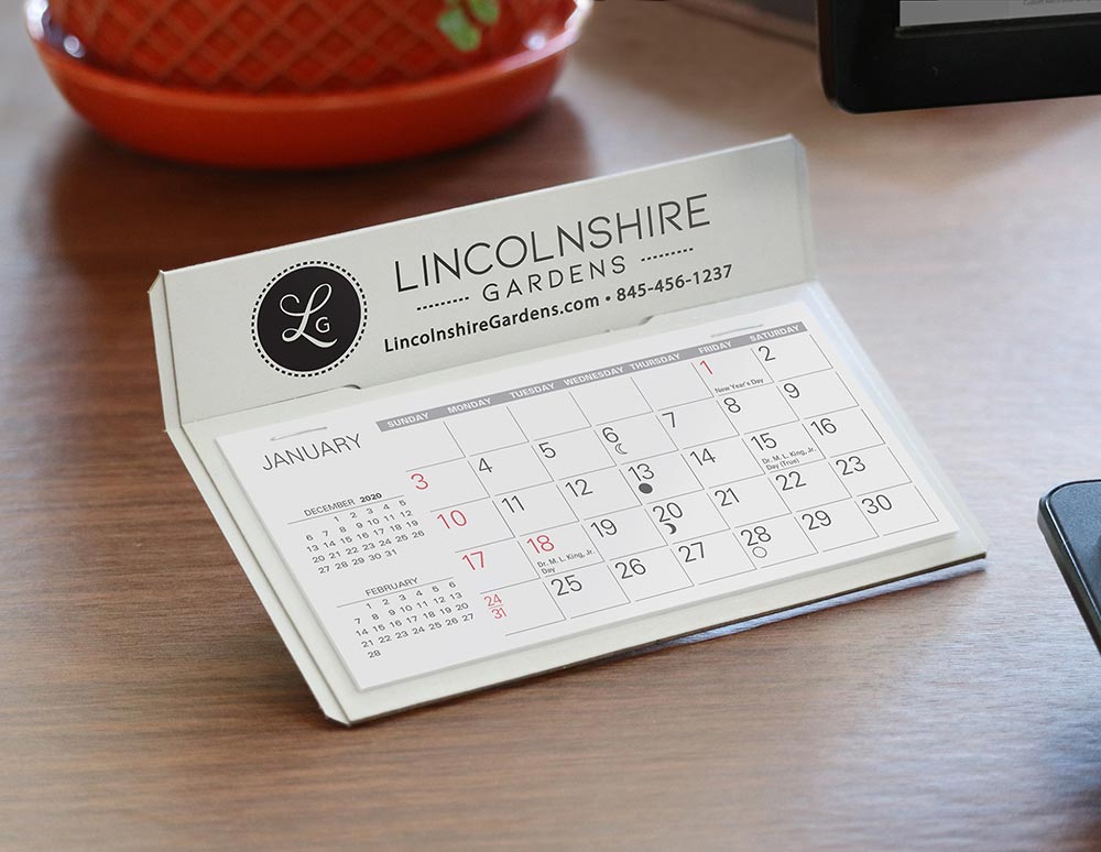 White cardboard desk calendar with company logo printed in black above the calendar pad