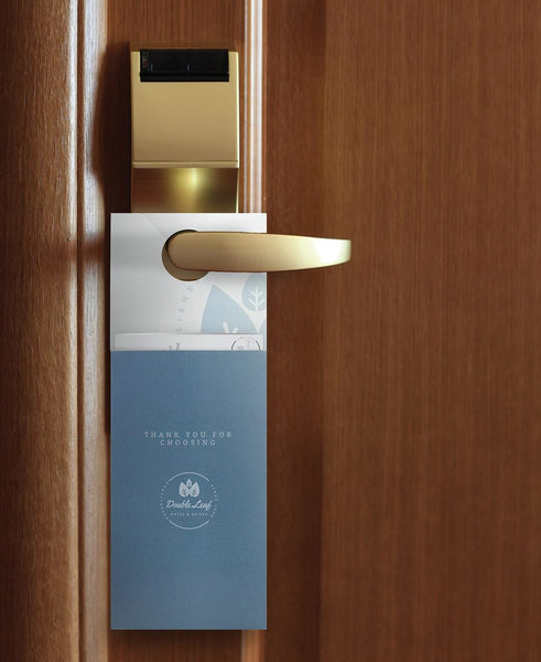 A hotel door hanger with pocket hangs on a lever-style gold door knob