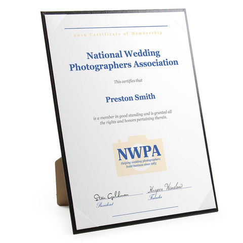 Vertical black frame has white ribbon corners to hold a certificate or award. Pop-out easel props up the frame.