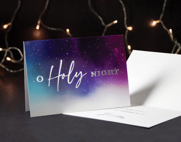 O Holy Night greeting card stands up while one lies on the desk with a silver foil imprint with a church logo.