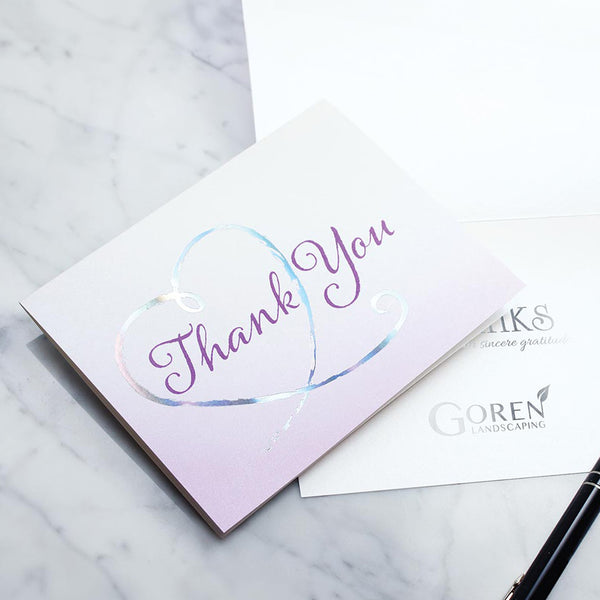 Purple gradient on card with purple thank you script circled by a holographic silver foil heart. The inside of another card shows a thank you sentiment with a company logo stamped in silver foil.