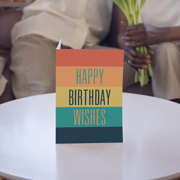 5 by 7 birthday wishes greeting card is propped on a white table in front of people sitting on a couch.