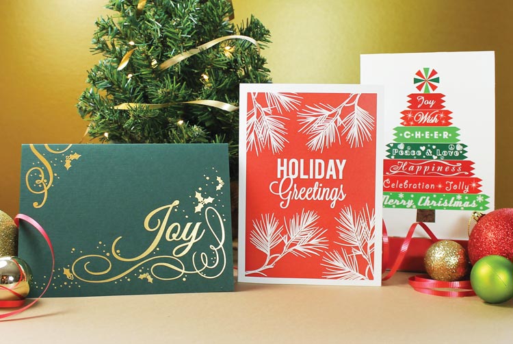 Three red, green, and white Christmas cards sit among holiday baubles and a small evergreen tree