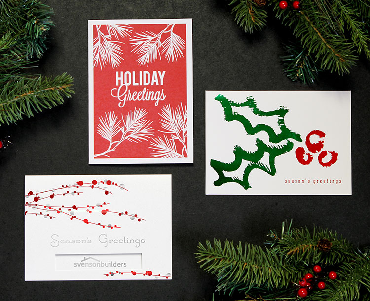 Three holiday cards with red and green designs. One has a company logo showing through a die-cut window.