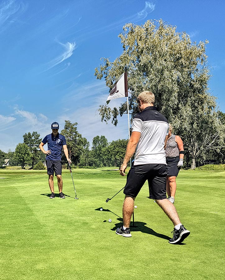 Three people surround the flag by the hole on a golf green