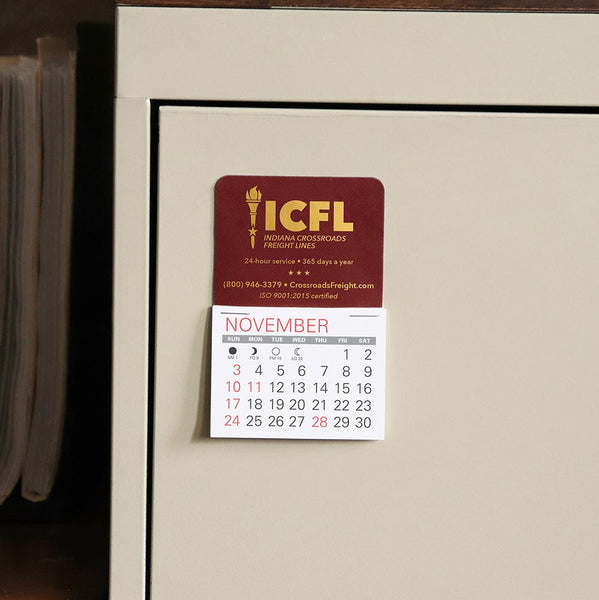 Maroon calendar with logistics company imprinted in gold foil sticks to a metal office cabinet drawer.