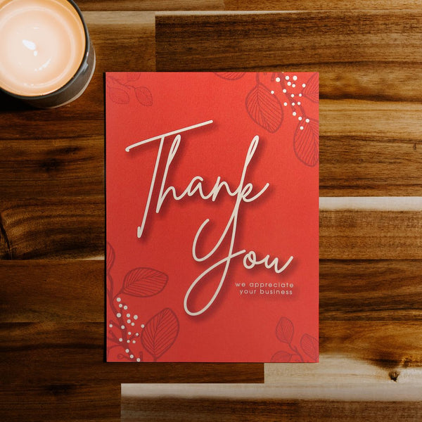 Recycled red thank you card for business on a wood desk next to a lit candle.