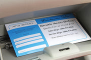 Blue and white promotional document pouch for a car dealership. Set in a glove box next to small metal tools.