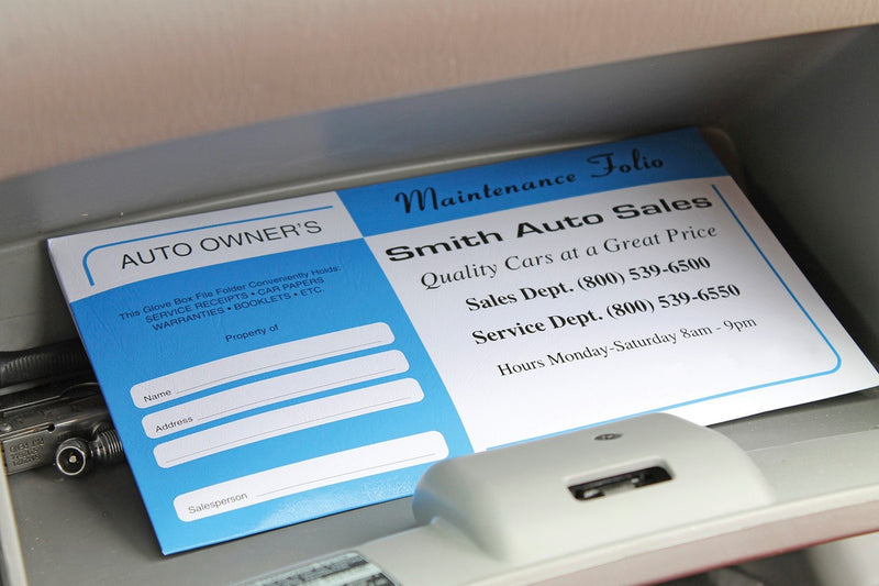 Blue and white promotional document pouch for a car dealership. Set in a glove box next to small metal tools.