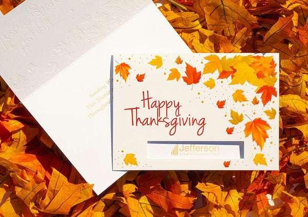 Thanksgiving greeting card with company logo sitting on a pile of orange autumn leaves